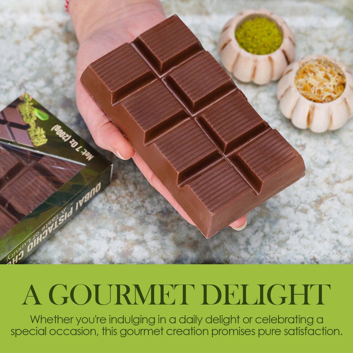 A hand holds a rectangular Crispy Dubai Chocolate Bar – 7 oz by Ceres Gourmet above a marble surface, with bowls of nuts nearby. Text below reads: Pure satisfaction—enjoy this gourmet treat daily or on special occasions.